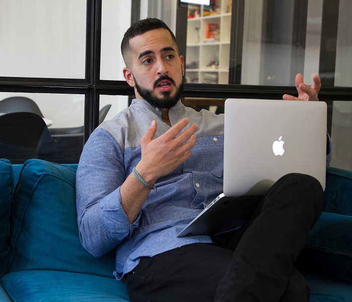 Man Sitting On A Blue Sofa Holding a Laptop Talking