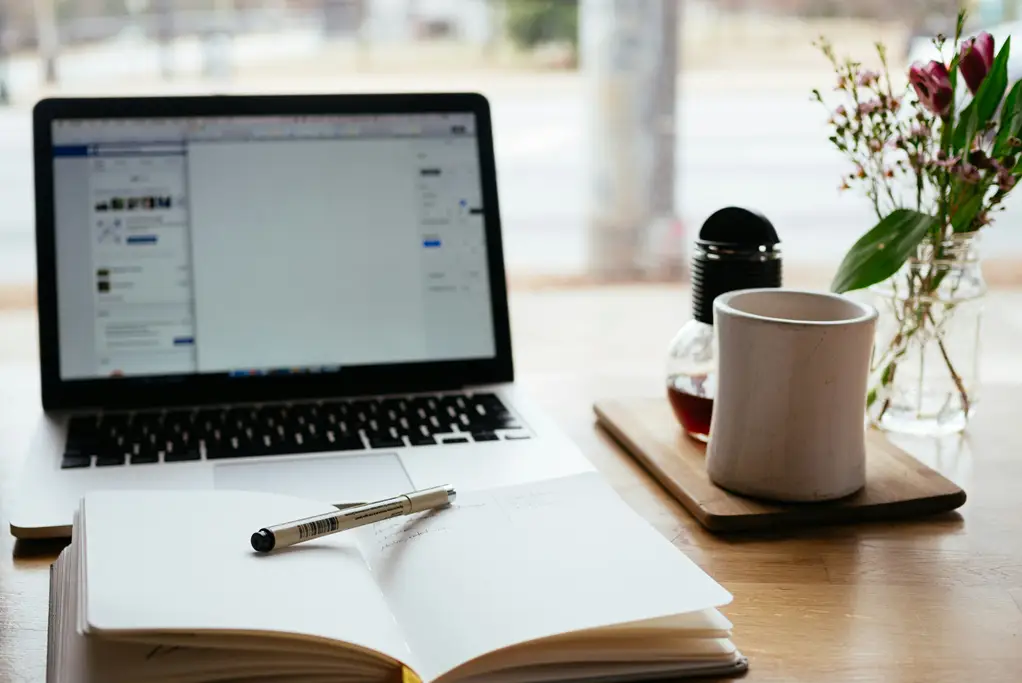 Laptop with Open Notebook And Cup of Coffee on a table